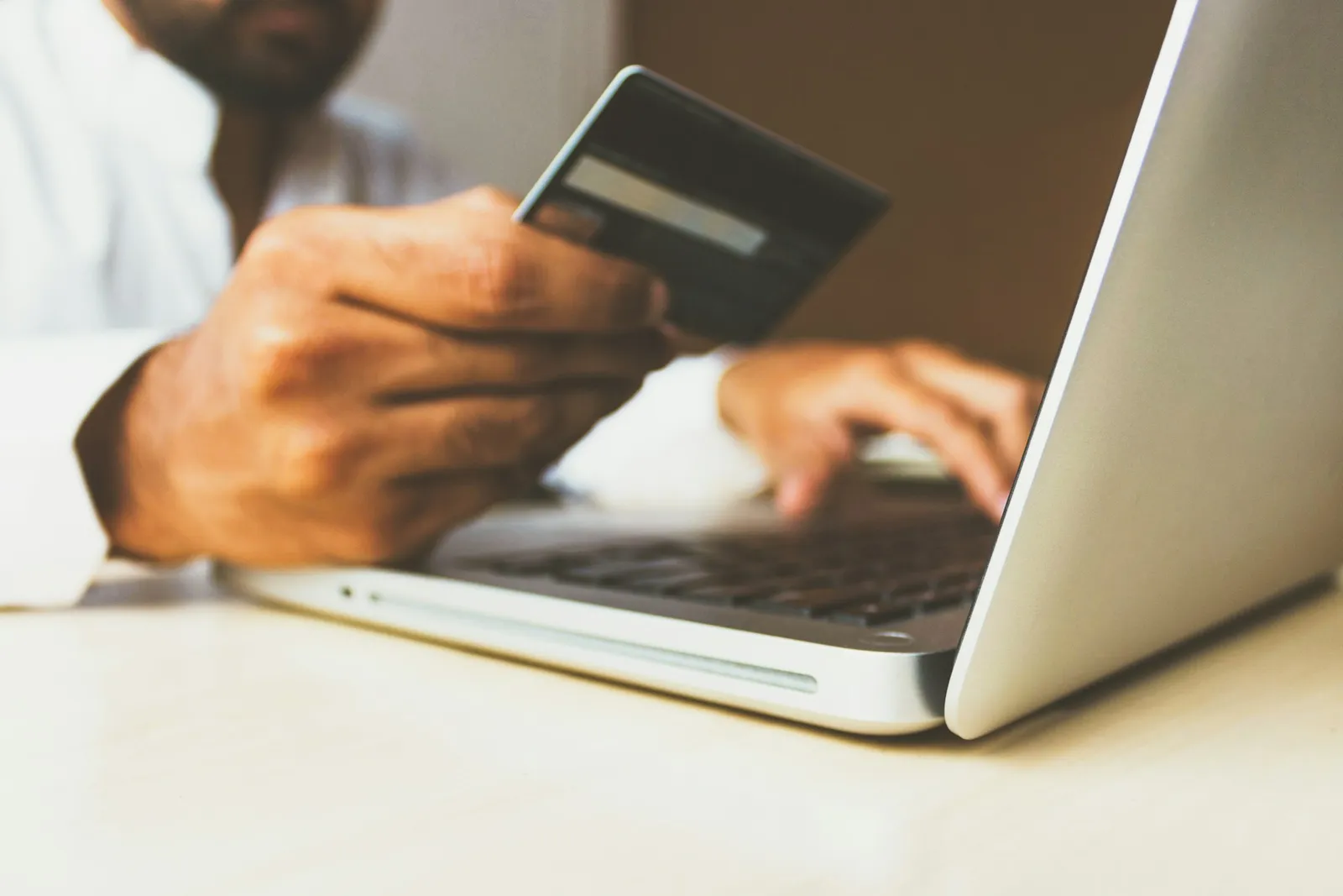 Hands typing on a laptop while holding a bank card.