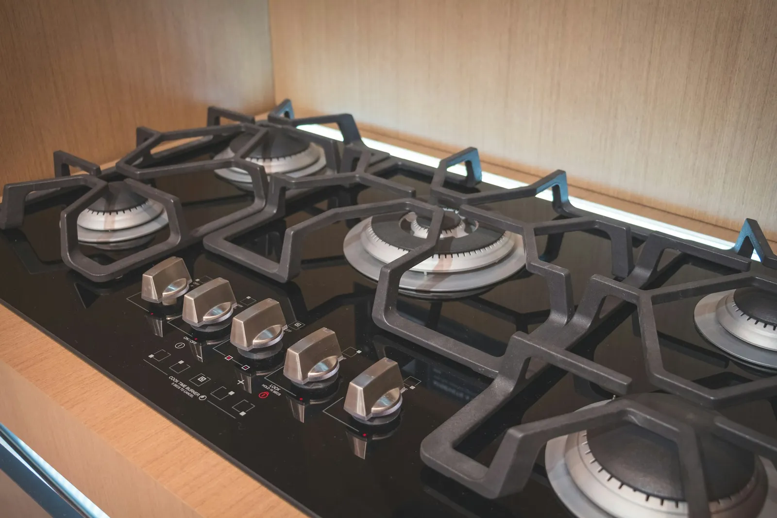 A black gas hob with five burners and a row of five control knobs along the front.