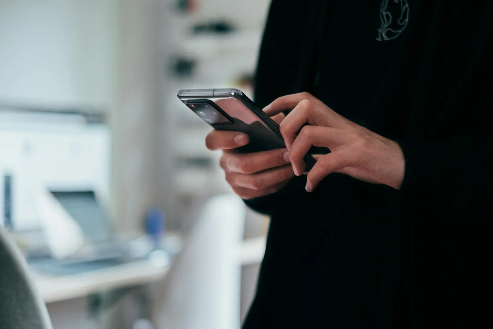 Hands holding a phone at a desk, thumb poised over the screen.